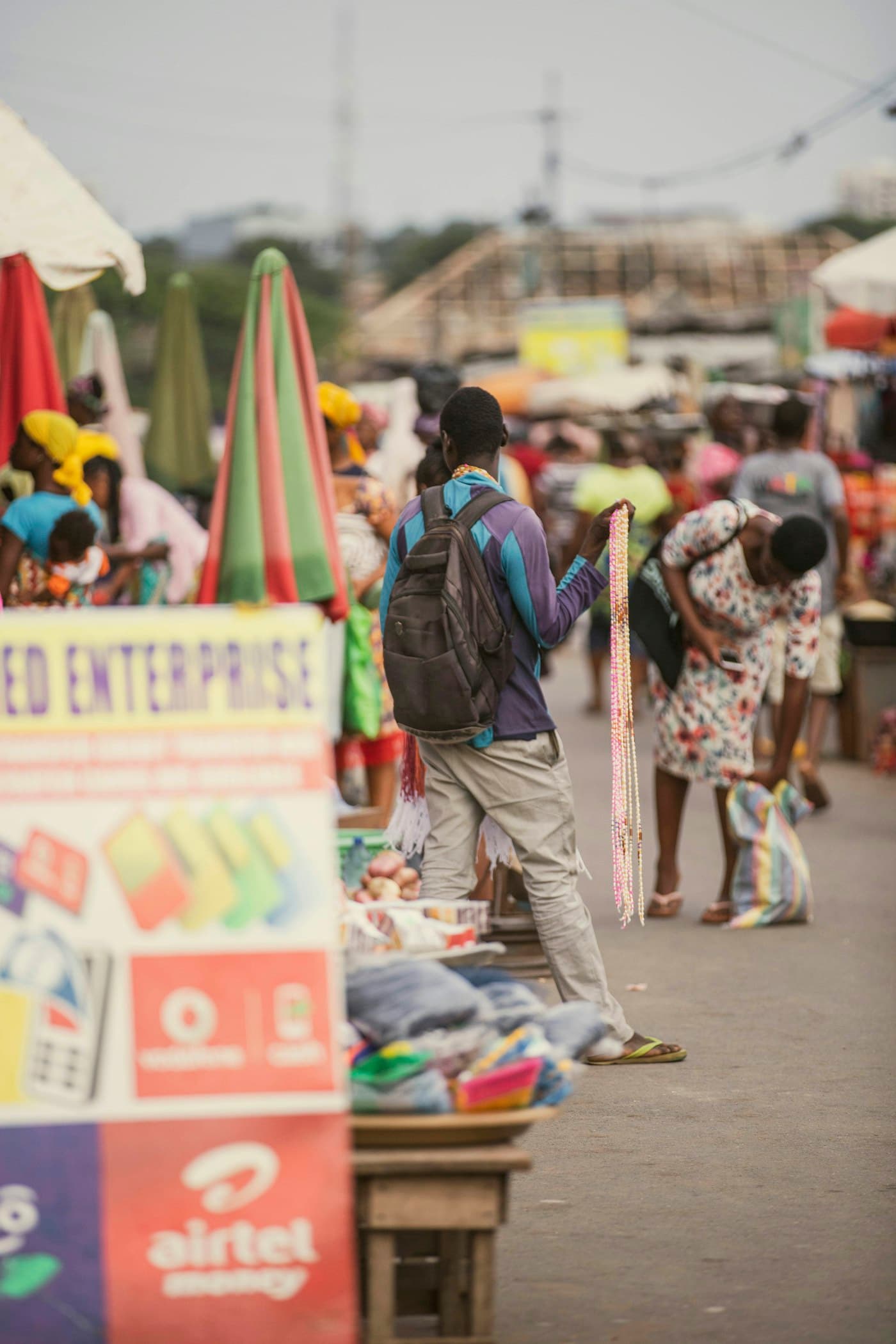 A Ghanaian market with bead sellers, umbrellas and mobile-money signs